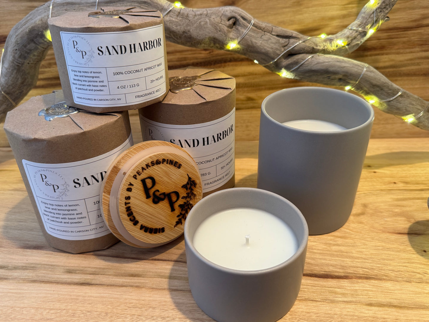 3 large 10oz Sand Harbor Candles and 2 small 4oz sand harbor candles. 3 are wrapped and sealed and 2 are unwrapped showing the gray ceramic and a branded wood lid.