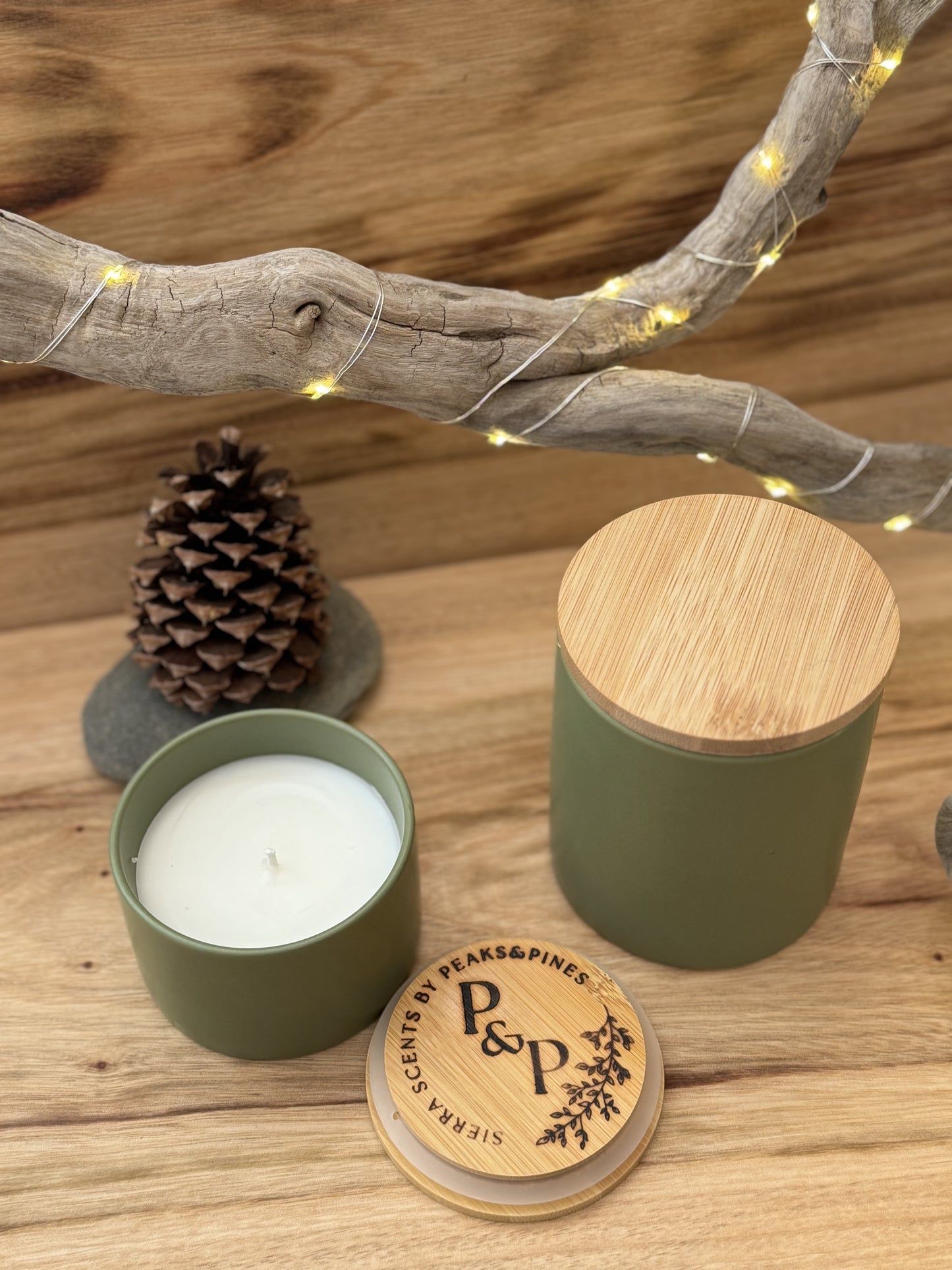 1 Emerald Bay 10 oz green ceramic candle and 1 4oz emerald bay green ceramic candle on a wood slab with a pine cone in the background. 