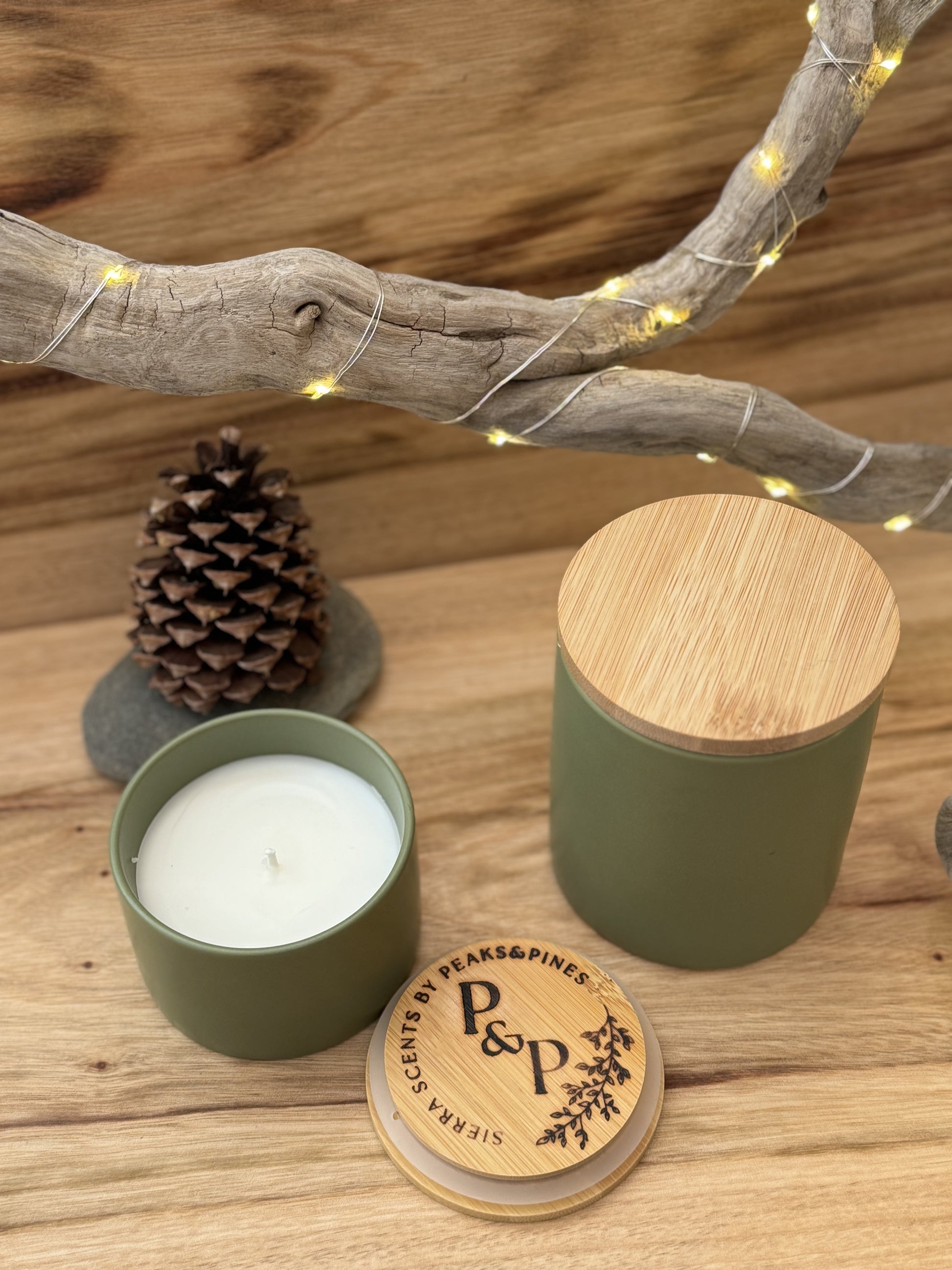 1 Emerald Bay 10 oz green ceramic candle and 1 4oz emerald bay green ceramic candle on a wood slab with a pine cone in the background. 