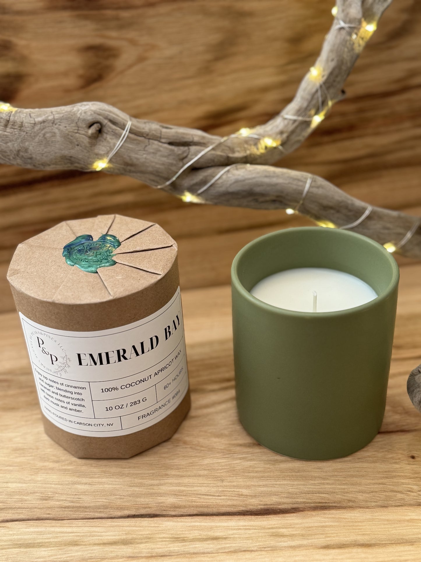 Two Emerald Bay 10 oz candles on a wooden surface, one wrapped in kraft paper with wax seal. The other shows the green ceramic vessel. 