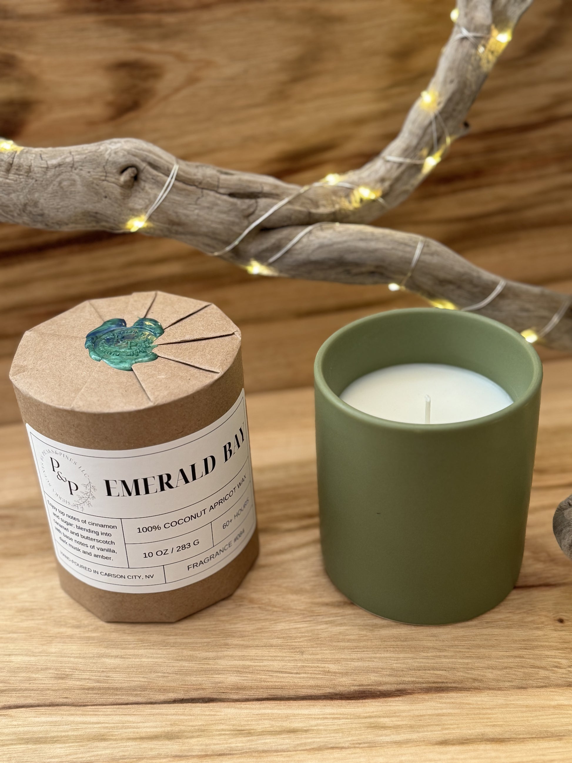 Two Emerald Bay 10 oz candles on a wooden surface, one wrapped in kraft paper with wax seal. The other shows the green ceramic vessel. 