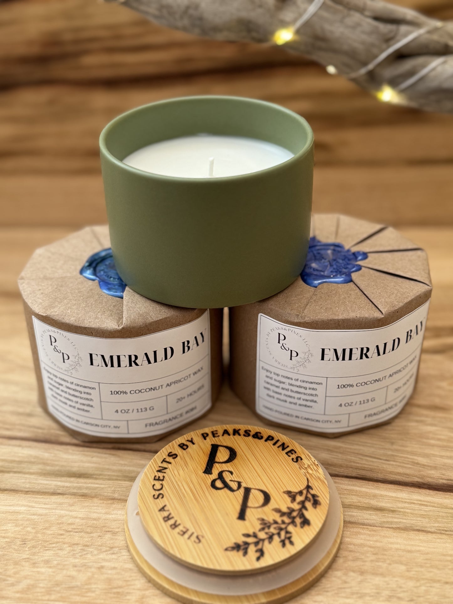 Three Emerald Bay 4 oz candles on a wooden surface, two wrapped in kraft paper with wax seal. One showing the green ceramic and branded wood lid.