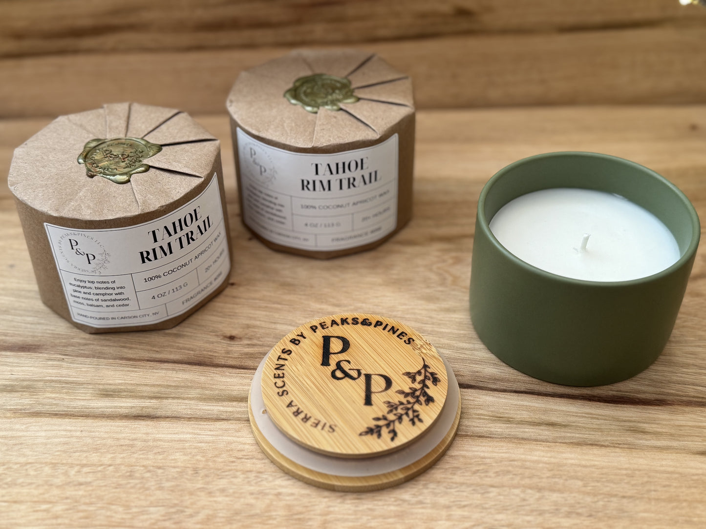 Three Tahoe Rim Trail 4 oz candles on a wooden surface, wrapped and unwrapped showing green ceramic jar and branded lid. 