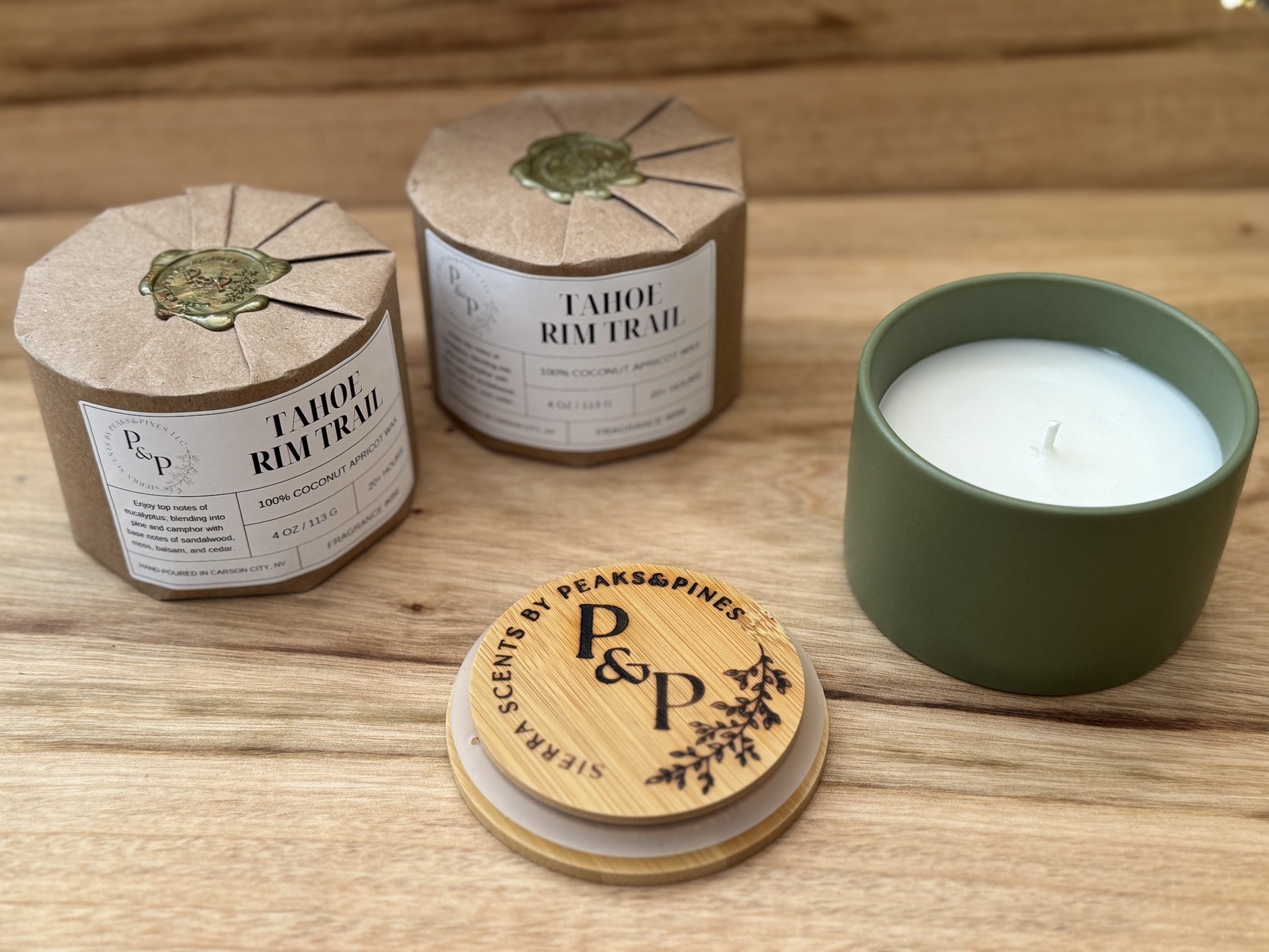 Three Tahoe Rim Trail 4 oz candles on a wooden surface, wrapped and unwrapped showing green ceramic jar and branded lid. 
