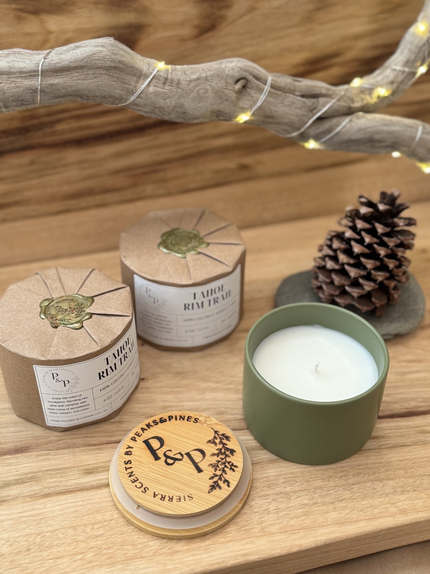 Three Tahoe Rim Trail 4 oz candles on a wooden surface, wrapped and unwrapped showing green ceramic jar. There is a pine cone in the background. 
