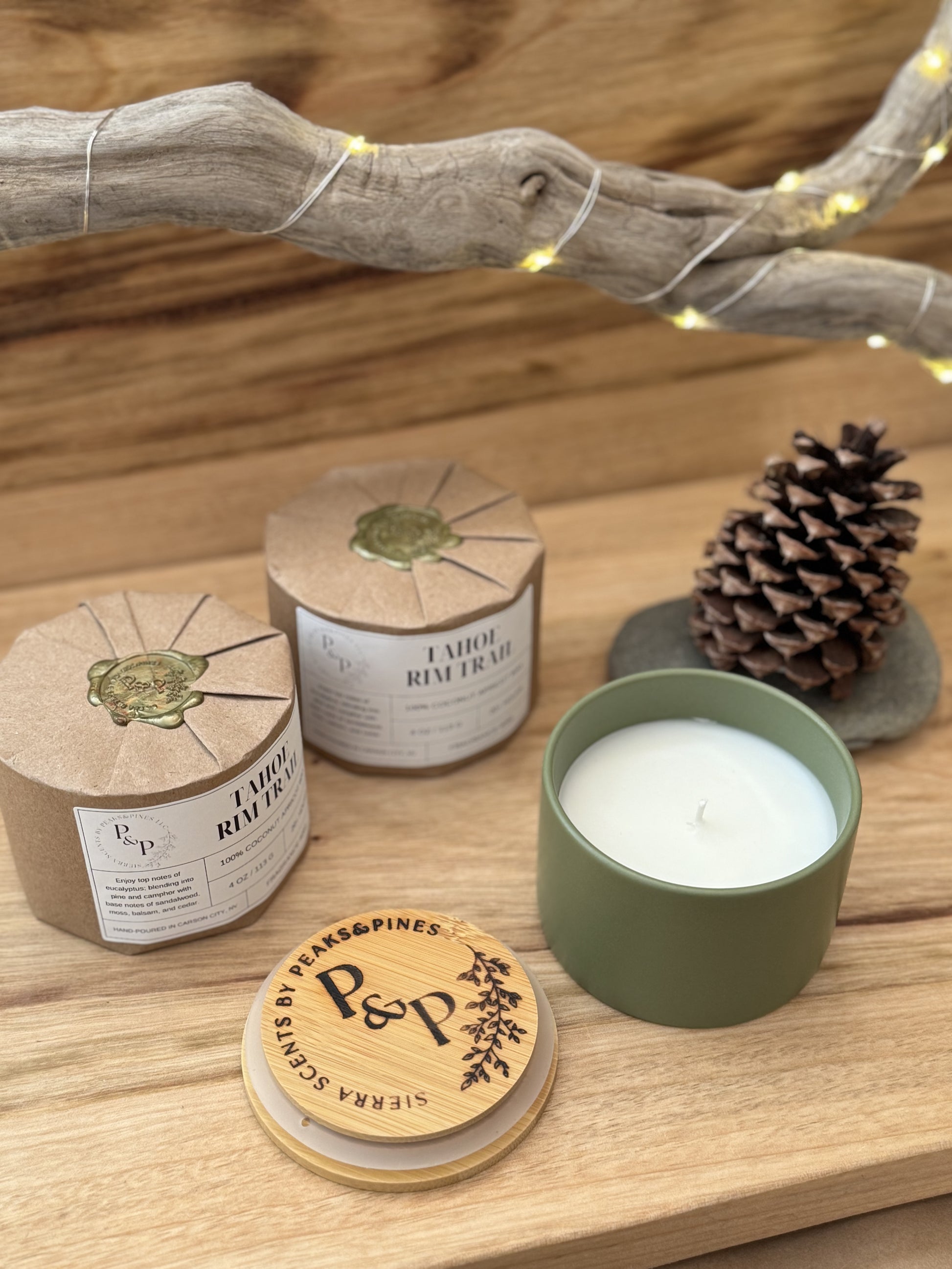 Three Tahoe Rim Trail 4 oz candles on a wooden surface, wrapped and unwrapped showing green ceramic jar. There is a pine cone in the background. 