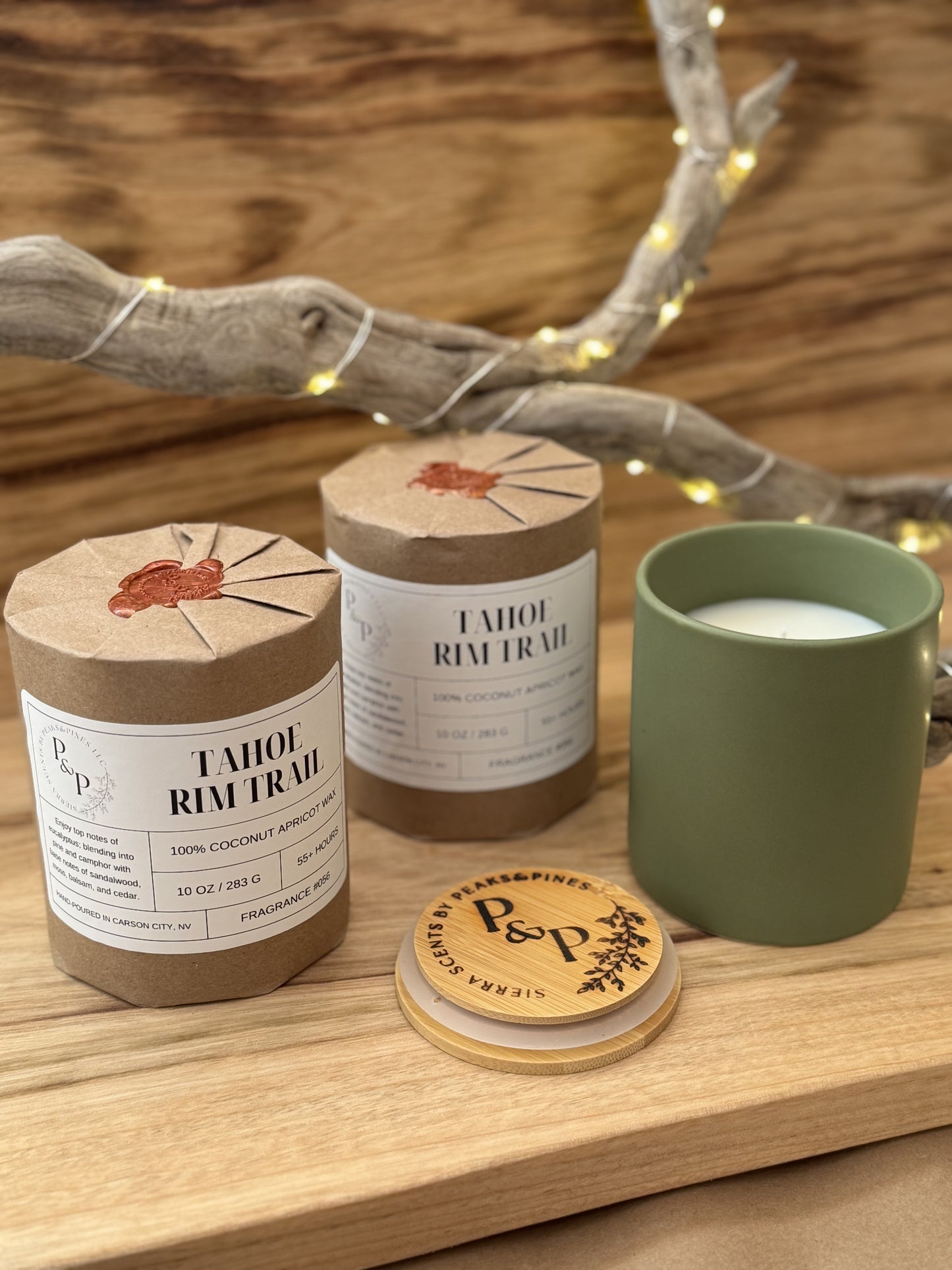 Three Tahoe Rim Trail 10 oz candles on a wooden surface, two wrapped in kraft paper with wax seal and one unwrapped showing the green ceramic and branded wood lid. 