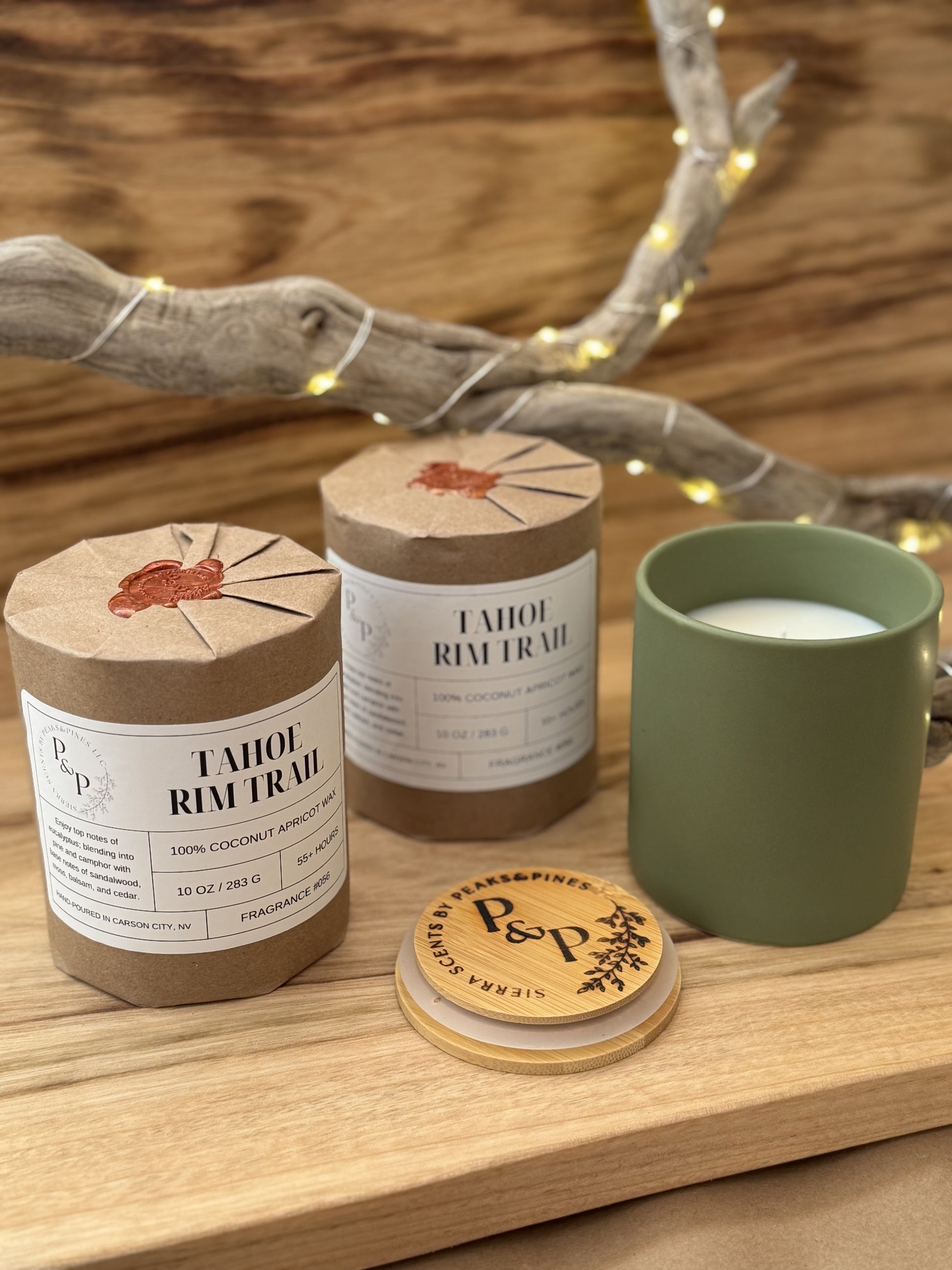 Three Tahoe Rim Trail 10 oz candles on a wooden surface, two wrapped in kraft paper with wax seal and one unwrapped showing the green ceramic and branded wood lid. 