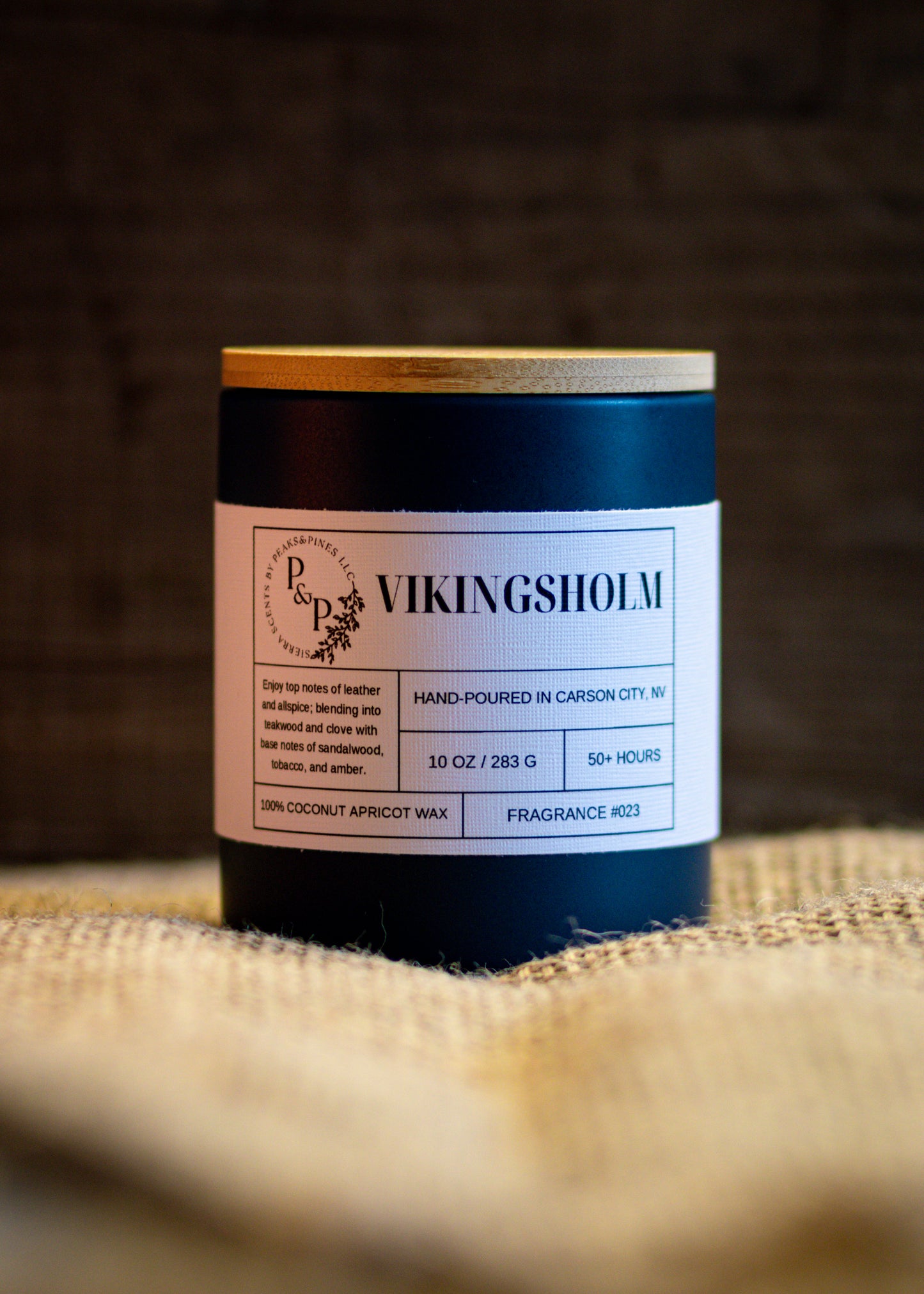Vikingsholm 10 oz ceramic candle by Peaks and Pines, blue ceramic jar with wood lid and white label on burlap. 