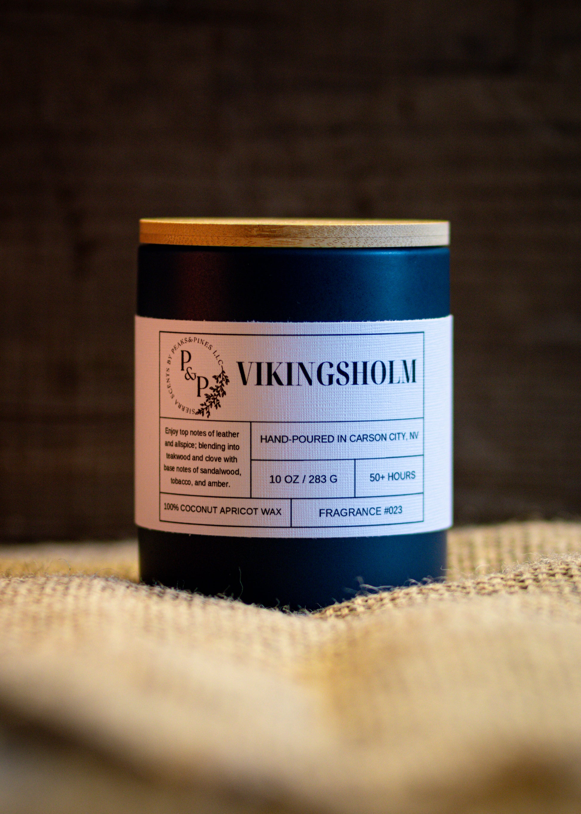 Vikingsholm 10 oz ceramic candle by Peaks and Pines, blue ceramic jar with wood lid and white label on burlap. 