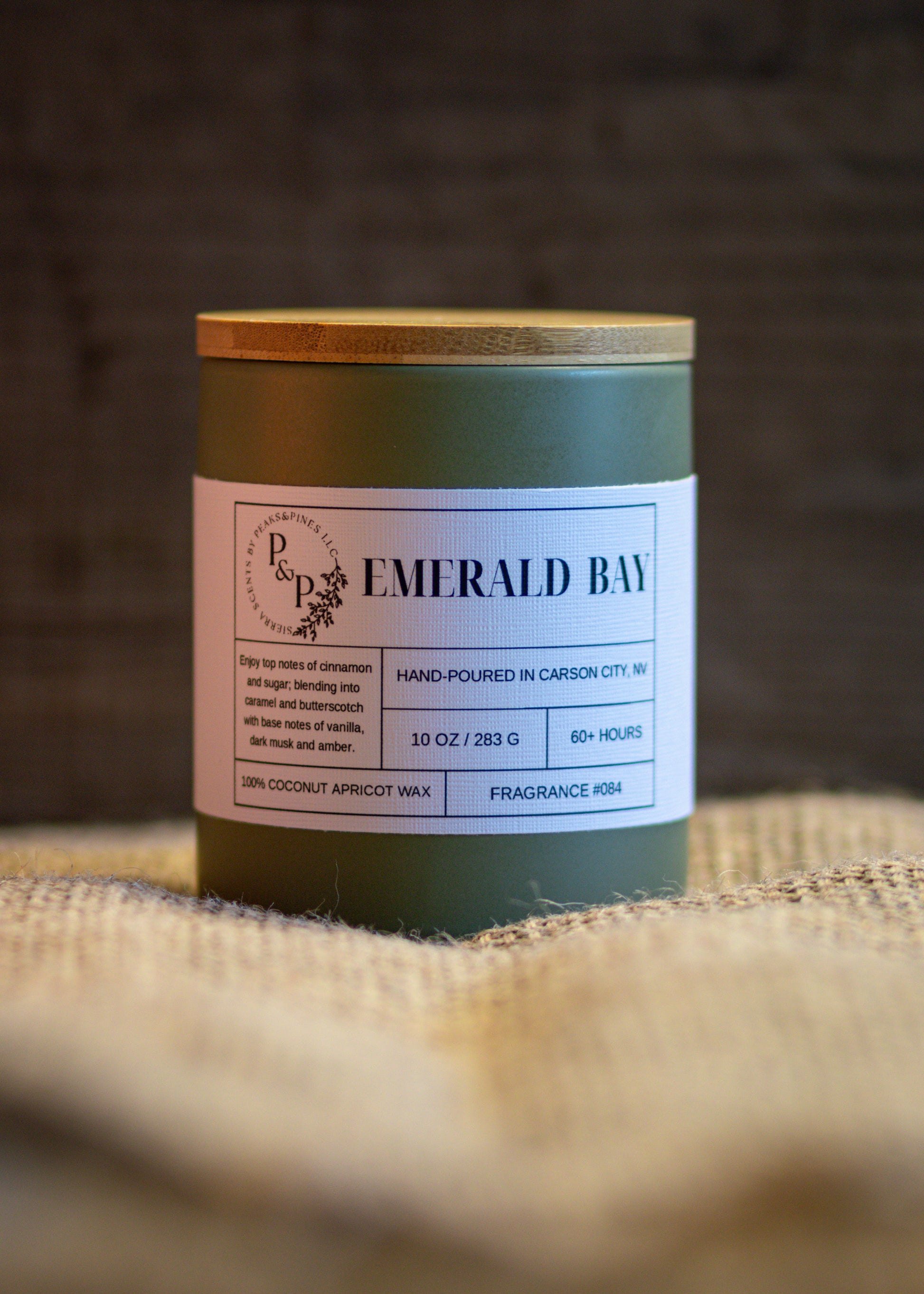 Emerald Bay 10 oz ceramic candle by Peaks and Pines, green ceramic jar with wood lid and white label on burlap.
