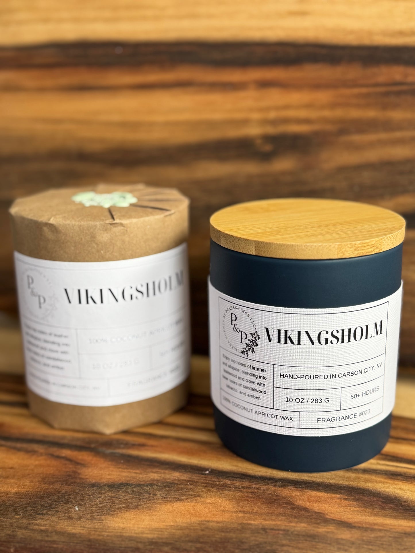 Two Vikingsholm 10 oz candles on a wooden surface, one wrapped in kraft paper with wax seal, the other showing the blue ceramic and white label. 