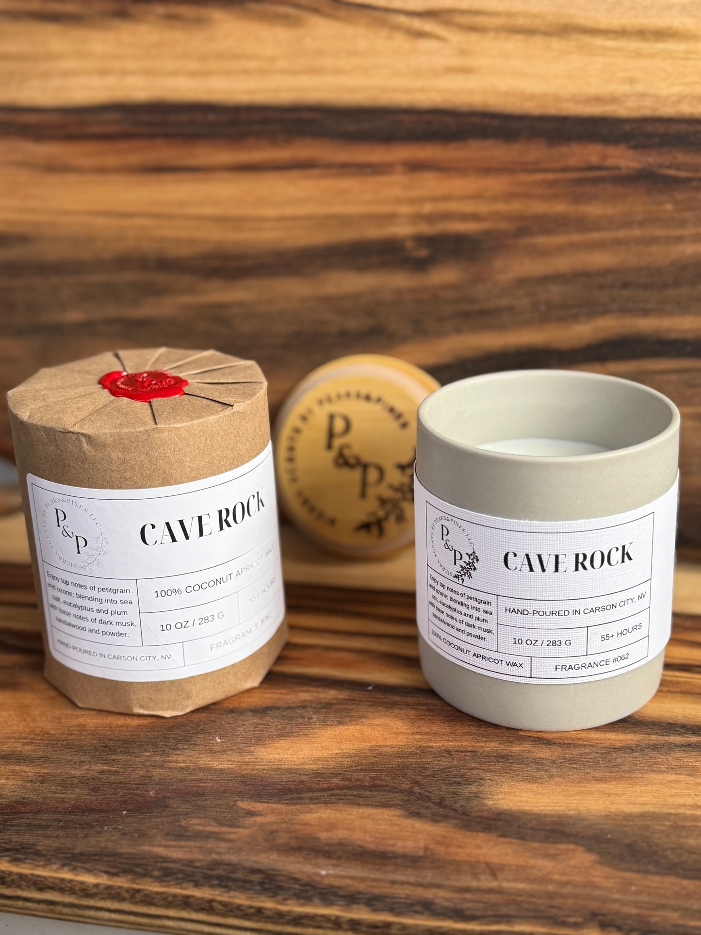 Two Cave Rock 10 oz candles on a wooden surface, one wrapped in kraft paper with wax seal