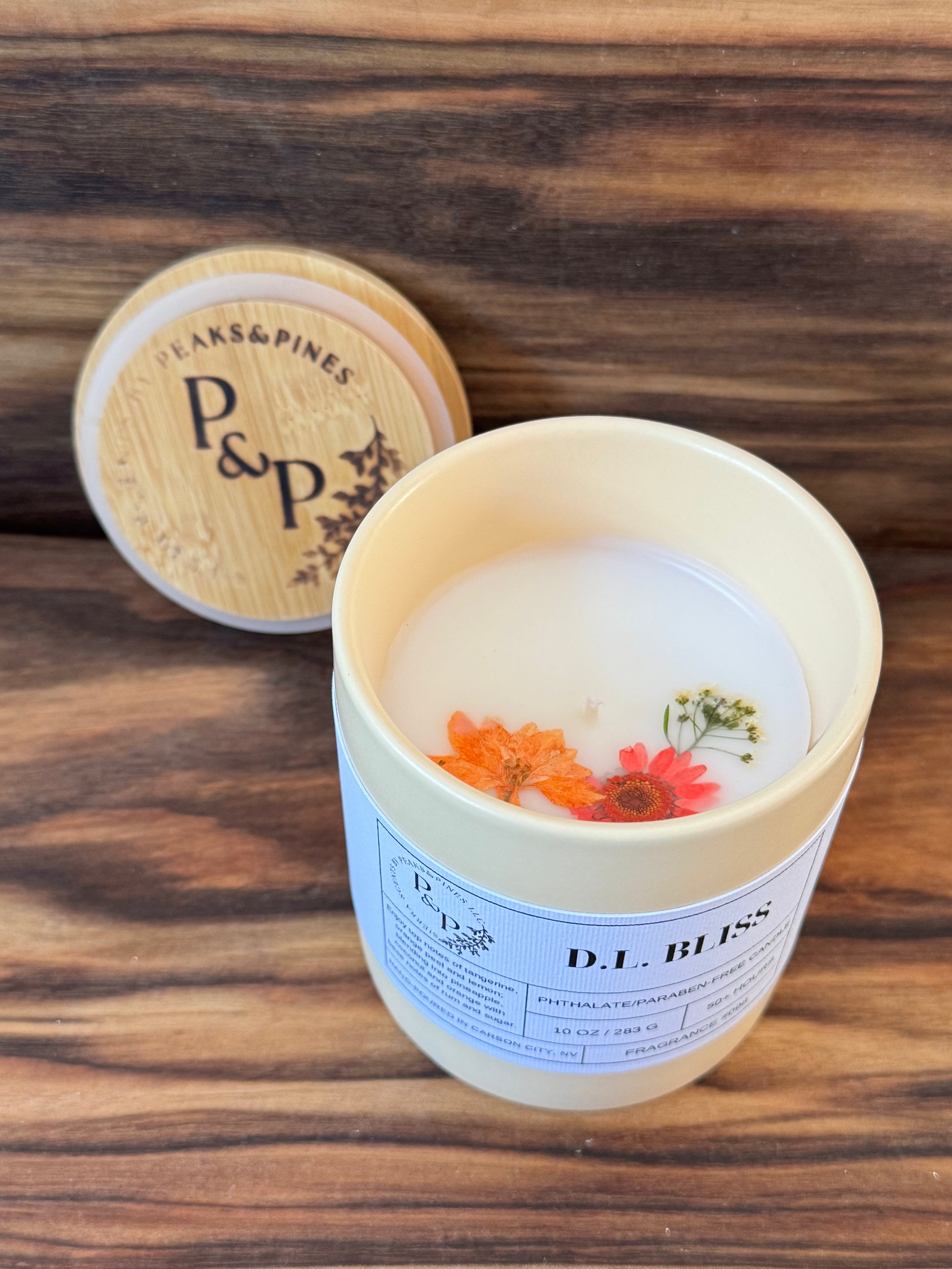 D.L. Bliss 10 oz  cream ceramic candle by Peaks and Pines, botanical impressions line with pressed flowers in the wax and branded wood lid
