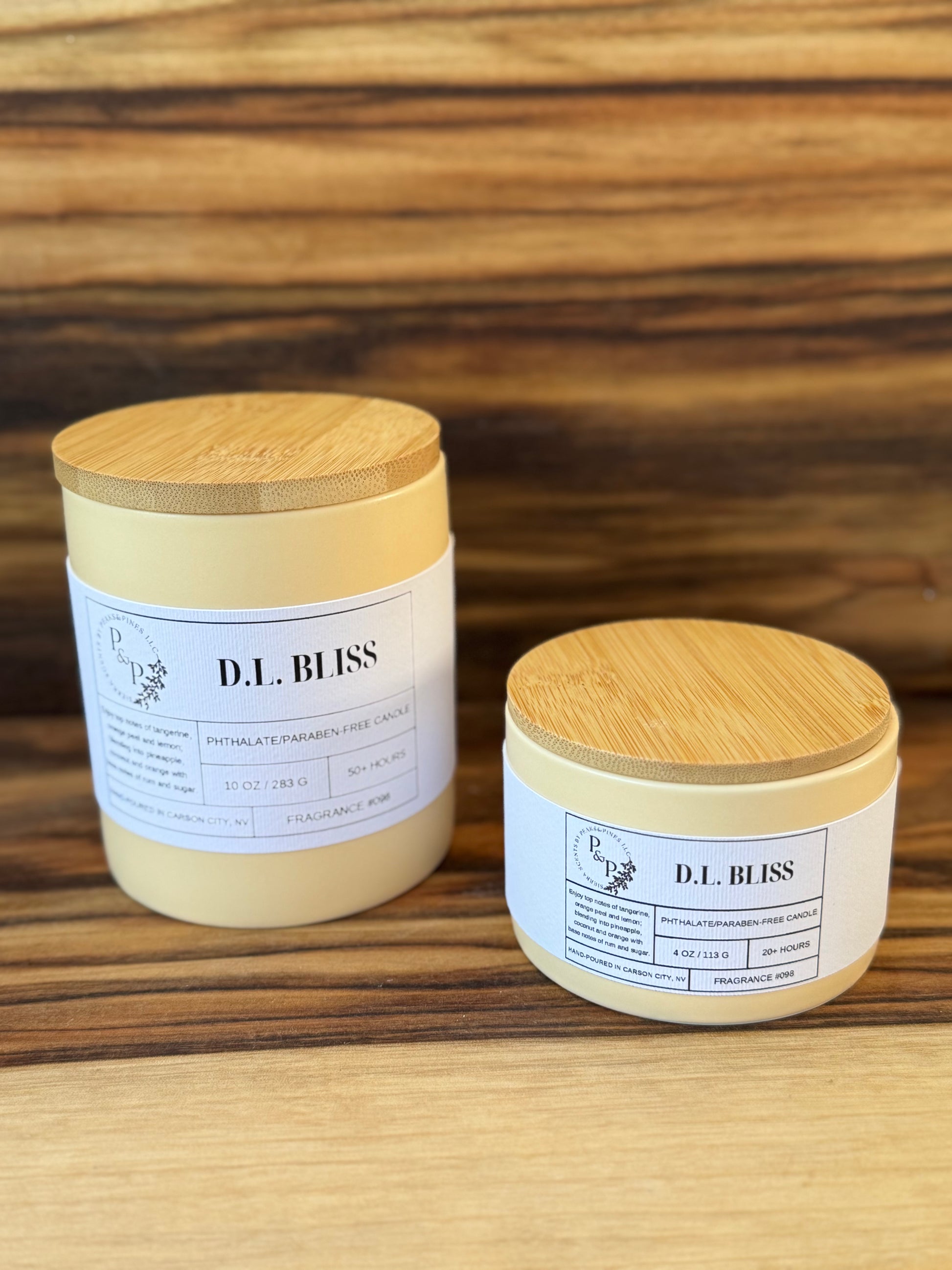 D.L. Bliss 4 oz and 10 oz ceramic candles from the Peaks and Pines botanical impressions line displayed together showing cream ceramic and white label.