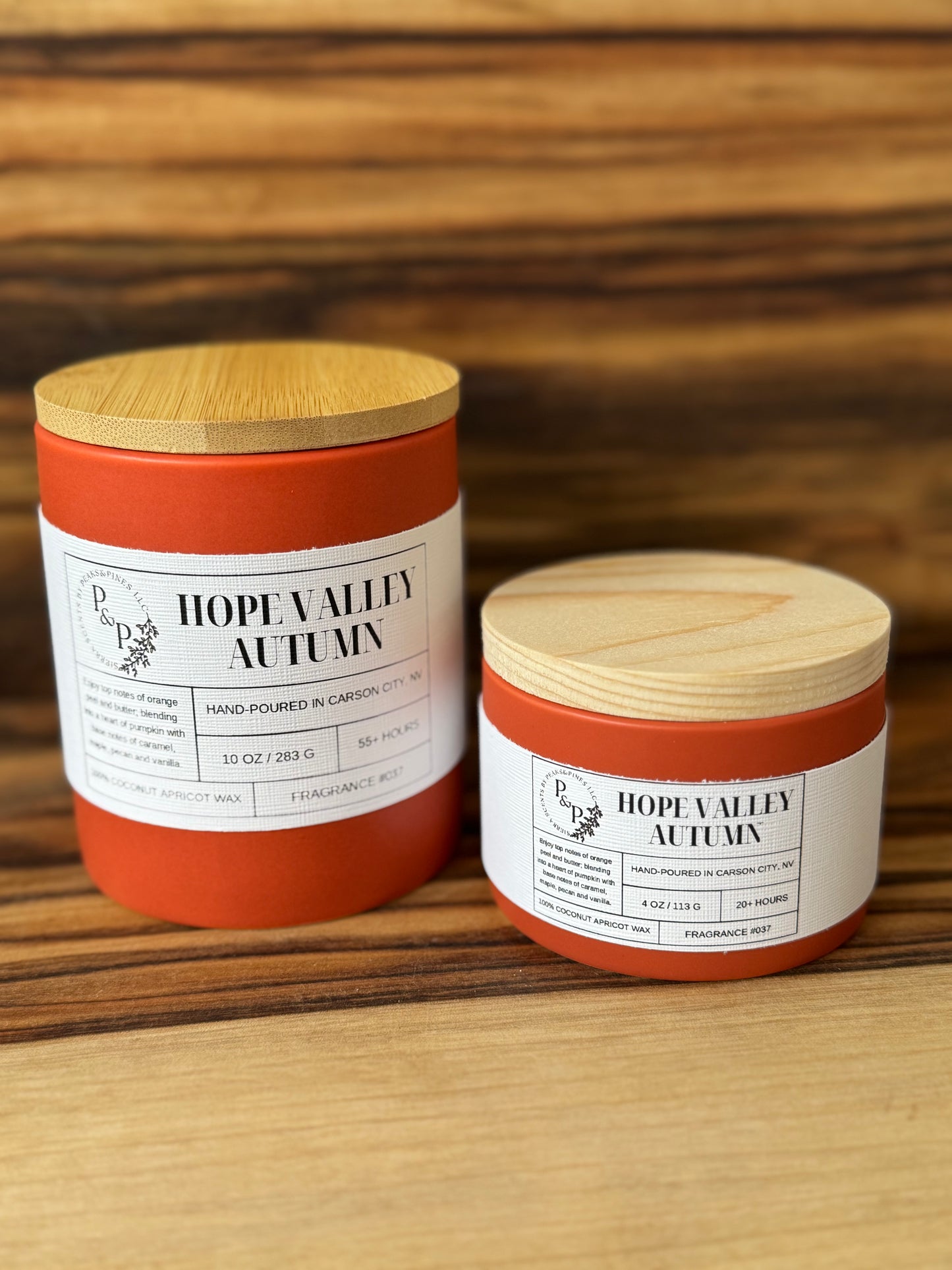 Hope Valley Autumn 10 oz and 4 oz ceramic candles displayed together. Both with orange ceramic vessels and white labels. 