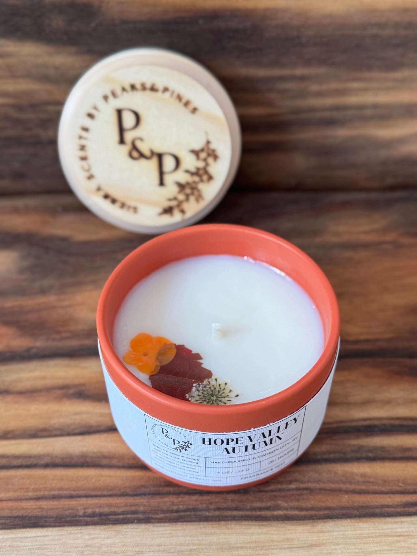 Hope Valley Autumn 4 oz orange ceramic candle by Peaks and Pines, with pressed flowers and leaves in the wax and branded wood lid