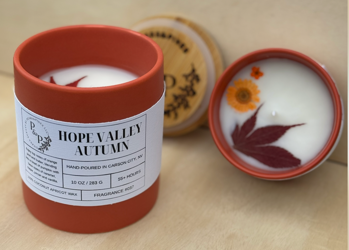 Hope Valley Autumn 10 oz and 4 oz ceramic candles displayed together. The 4oz shows the pressed leaves and flowers in the wax with a branded wood lid in the back. 