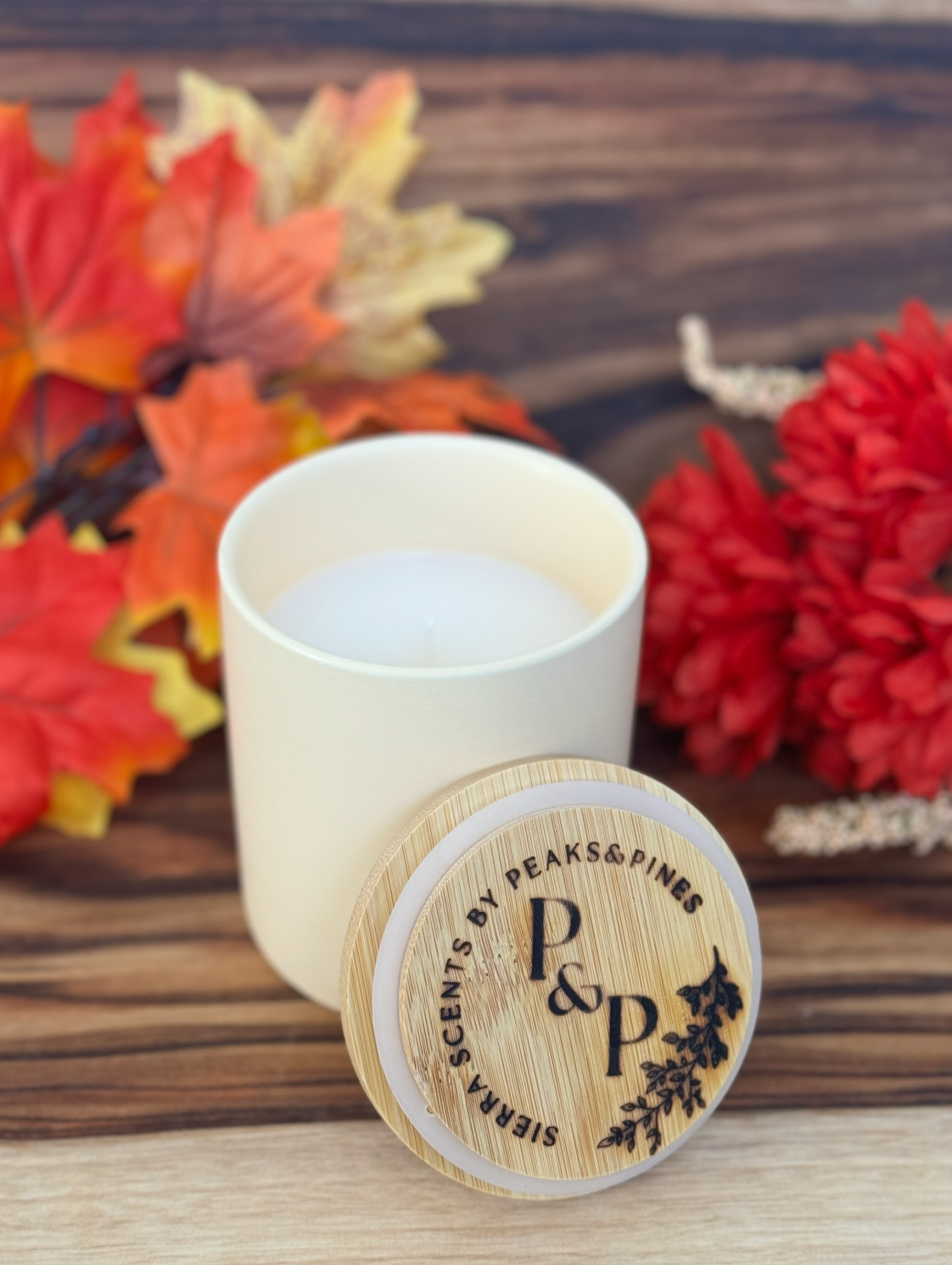Cream Apple Hill Harvest candle displayed in front of fall leaves and on a wood surface. 