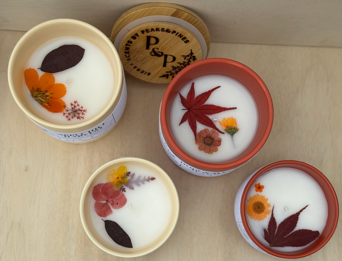 Apple Hill Harvest 10 oz and 4 oz cream ceramic candles and Hope Valley Autumn 10 oz and 4 oz orange ceramic candles. Image shows the pressed flowers and leaves in the wax of all 4 candles.  